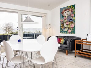 A modern dining area with a round table and white chairs, a black leather sofa, and a colorful artwork on the wall. - 6 Person Holiday Home in Borkop (Borkop)