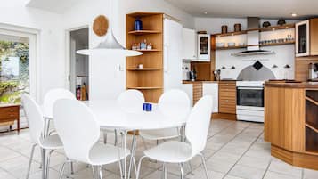 Una cocina moderna con armarios blancos, una isla central y un comedor con sillas blancas.