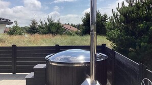 A hot tub with a tall, cylindrical chimney, surrounded by a wooden deck and a black fence. - Luxury Spa Retreat in Vejers - By Traum Ferienwohnungen (Vejers Strand)