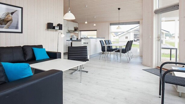 Un intérieur moderne avec un canapé en cuir noir, une table blanche et un coin repas avec des chaises.