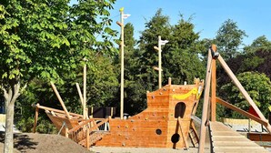 Une structure de jeu en bois qui ressemble à un navire, avec des prises d’escalade et un toboggan.