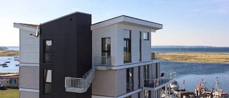 Un edificio moderno de varios pisos con un balcón, situado cerca de un cuerpo de agua con barcos.