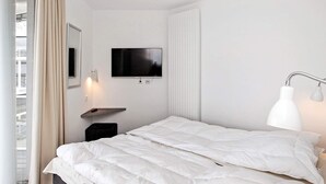 A modern hotel room with a bed, a television mounted on the wall, a bedside table, and a window with curtains. - Holiday Home in Wendtorf (Wendtorf)