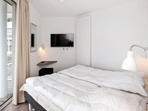 A modern hotel room with a bed, a television mounted on the wall, a bedside table, and a window with curtains.