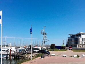 A marina with boats docked, a flagpole with a flag, and a modern building under construction. - Holiday Home in Wendtorf (Wendtorf)