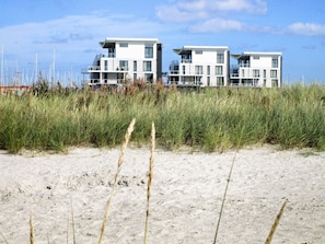 A beachfront property with modern architecture, featuring multiple balconies and a sandy foreground. - Holiday Home in Wendtorf (Wendtorf)