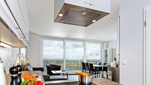 A modern kitchen with a built-in stove, large windows, and a dining area with a view. - Holiday Home in Wendtorf (Wendtorf)