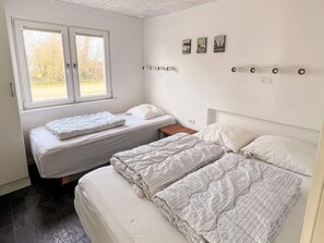 Un dormitorio con dos camas, una ventana y una estantería de pared con fotografías.