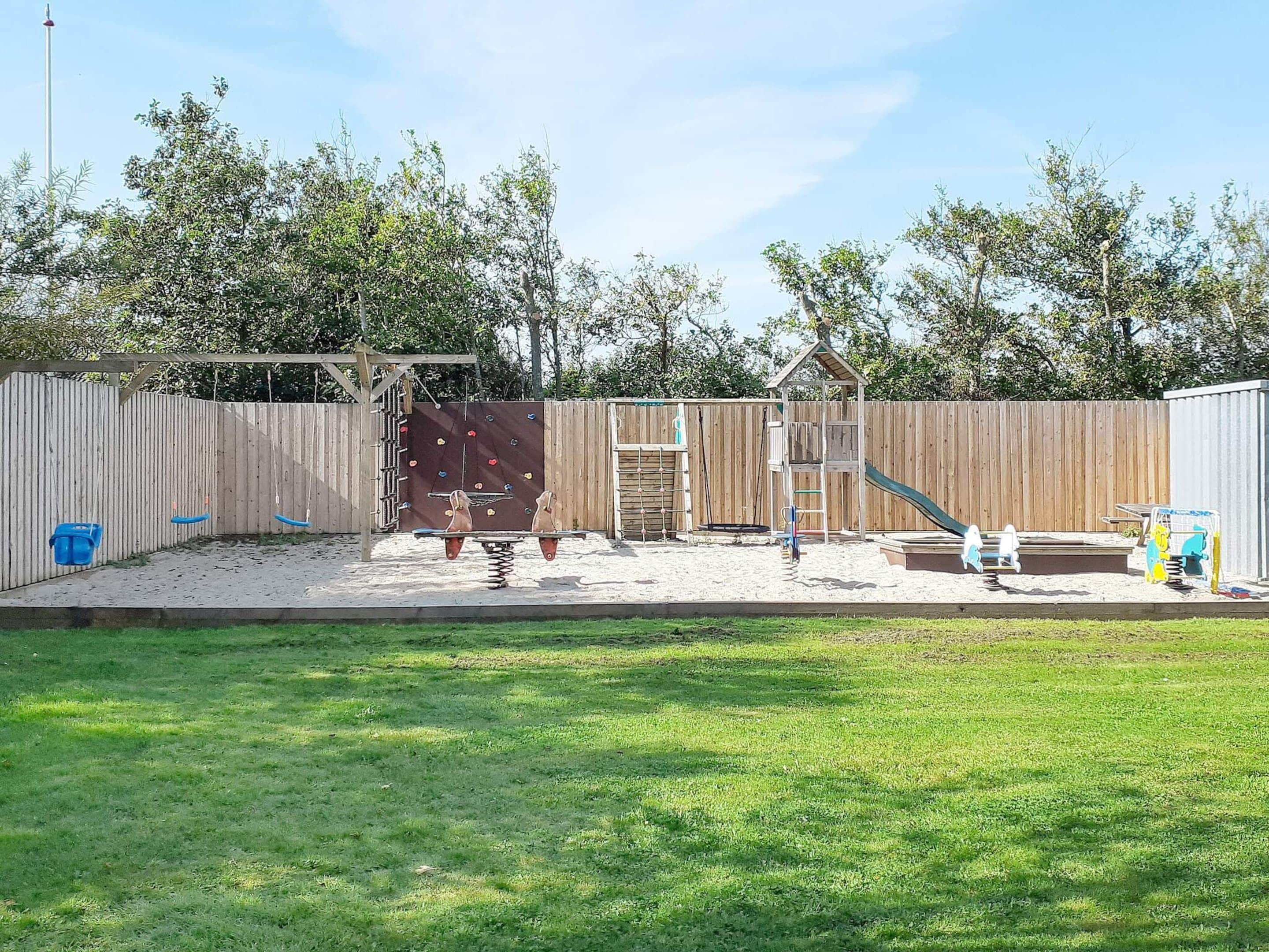 A fenced backyard with a swing set, a slide, and a small playhouse.
