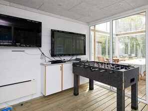 Una habitación con mesa de fútbol de mesa, un televisor montado en la pared y un amplio ventanal con vistas al exterior.