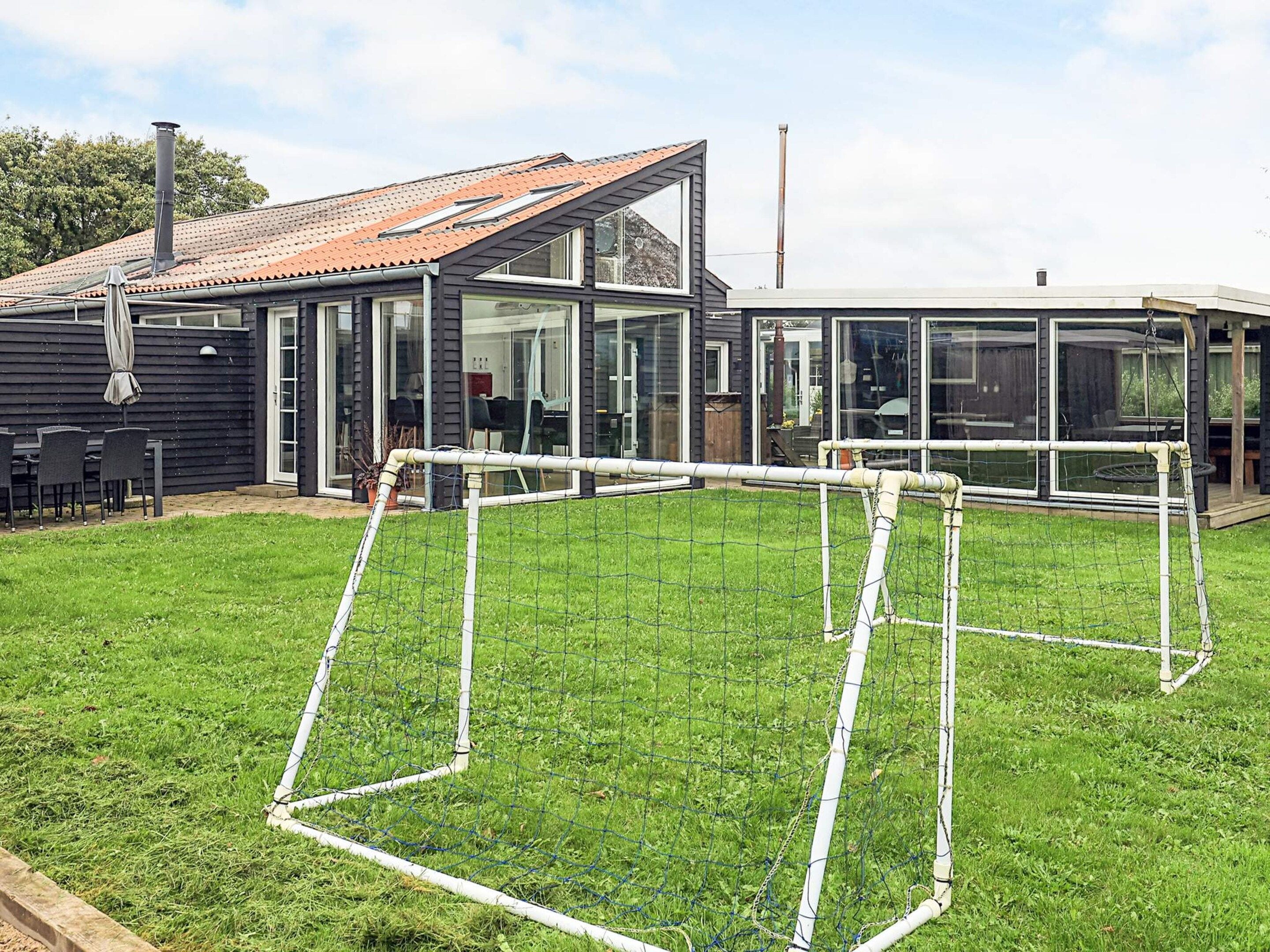 A modern house with a glass conservatory, a fenced backyard, and a patio area.