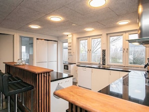 A kitchen with a central island, bar stools, white cabinets, and a window with a view. - 4 Star Holiday Home in Vinderup (Vinderup)