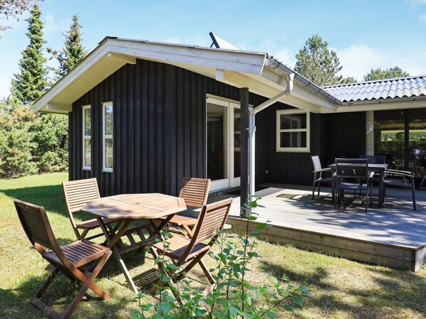 A wooden deck with a table and chairs, a covered patio area, and a view of a forested landscape.