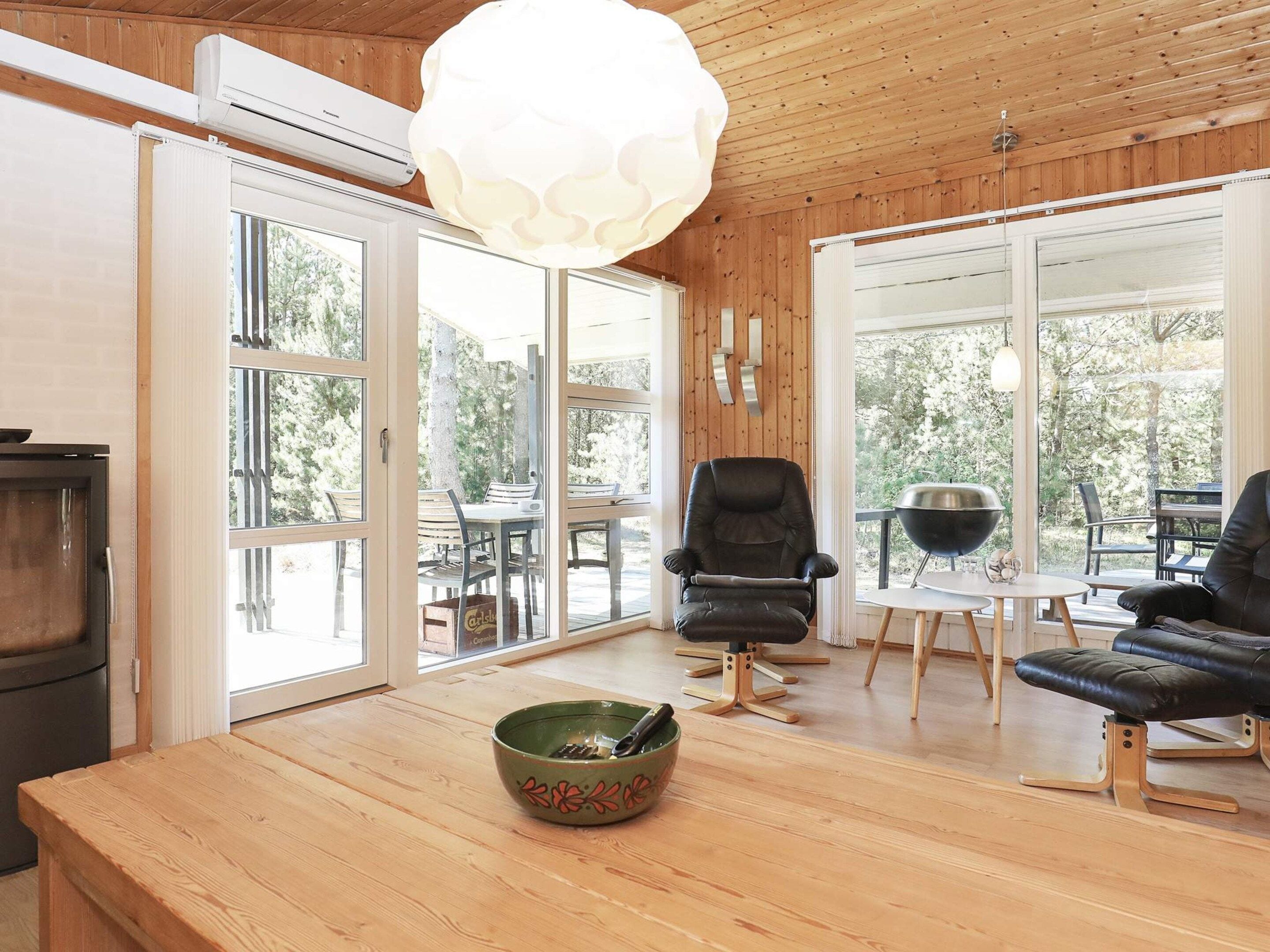 A modern interior with wooden flooring, a dining area with a table and chairs, a black leather sofa, and a large window providing a view of the outdoors.