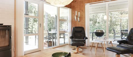 A modern interior with wooden flooring, a dining area with a table and chairs, a black leather sofa, and a large window providing a view of the outdoors.