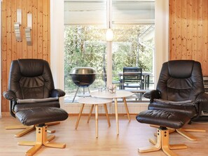 A room with two leather chairs, a round table, a grill, and a view of trees through a window. - 6 Person Holiday Home in Jerup (Jerup)