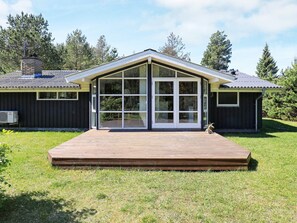 A modern house with a large glass door entrance, a wooden deck, and a chimney. - 6 Person Holiday Home in Jerup (Jerup)