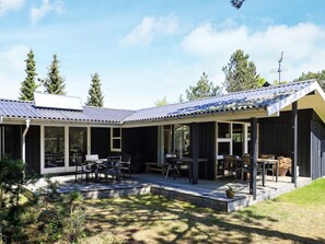 A modern house with a covered patio, large windows, and a well-maintained lawn.