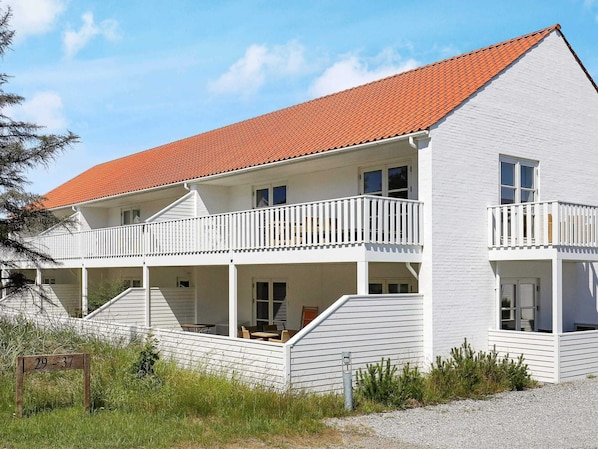 A two-story white building with a red-tiled roof, multiple balconies, and a covered outdoor seating area.