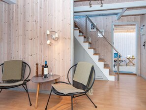 A modern interior with a wooden wall, a staircase, two wicker chairs, a small table with a bottle and glass, and a view of a balcony. - Quaint Holiday Home in Hemmet near Fjord (Hemmet)