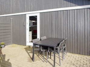 Un patio con una mesa y sillas, una puerta que da a una habitación con estantes, y una planta pequeña en maceta.