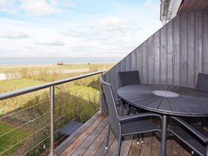 Un balcon avec une table et des chaises, donnant sur une zone herbeuse et un plan d’eau.