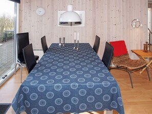 A dining area with a table set for four, surrounded by chairs, a clock on the wall, and a window providing a view outside.
