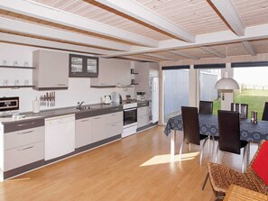 Une cuisine moderne avec des meubles blancs, un coin repas comprenant une table et des chaises, et une vue sur l’extérieur.