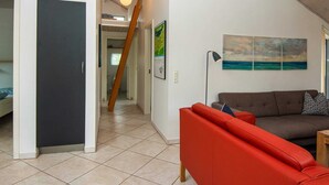 A modern living room with a red sofa, a brown sofa, and a painting of a beach scene. There is a staircase leading to another room. - 8 Person Holiday Home in Brovst (Brovst)