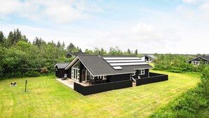 A modern black house with a large deck, surrounded by a well-maintained lawn and dense forest. - 8 Person Holiday Home in Brovst (Brovst)