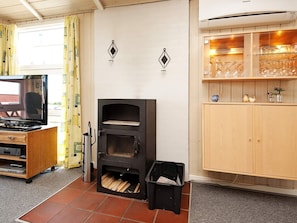 A room with a fireplace, a television, a cabinet with glassware, and a window with curtains. - 4 Star Holiday Home in Sjolund (Sjølund)