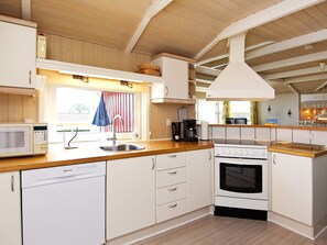A compact kitchen with white cabinetry, a built-in microwave, a stove, and a sink. - 4 Star Holiday Home in Sjolund (Sjølund)