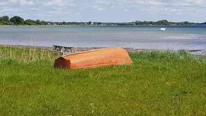A grassy area with a large orange structure, a body of water, and distant land with trees and buildings. - 4 Star Holiday Home in Sjolund (Sjølund)