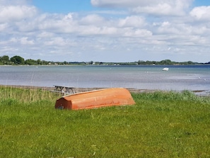 A grassy area with a large orange structure, a body of water, and distant land with trees and buildings. - 4 Star Holiday Home in Sjolund (Sjølund)