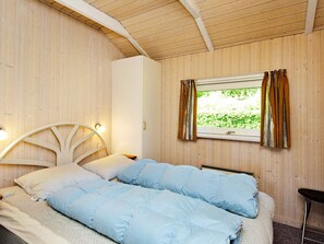 Quarto com cama, mesa de cabeceira, janela com cortinas e teto de madeira.