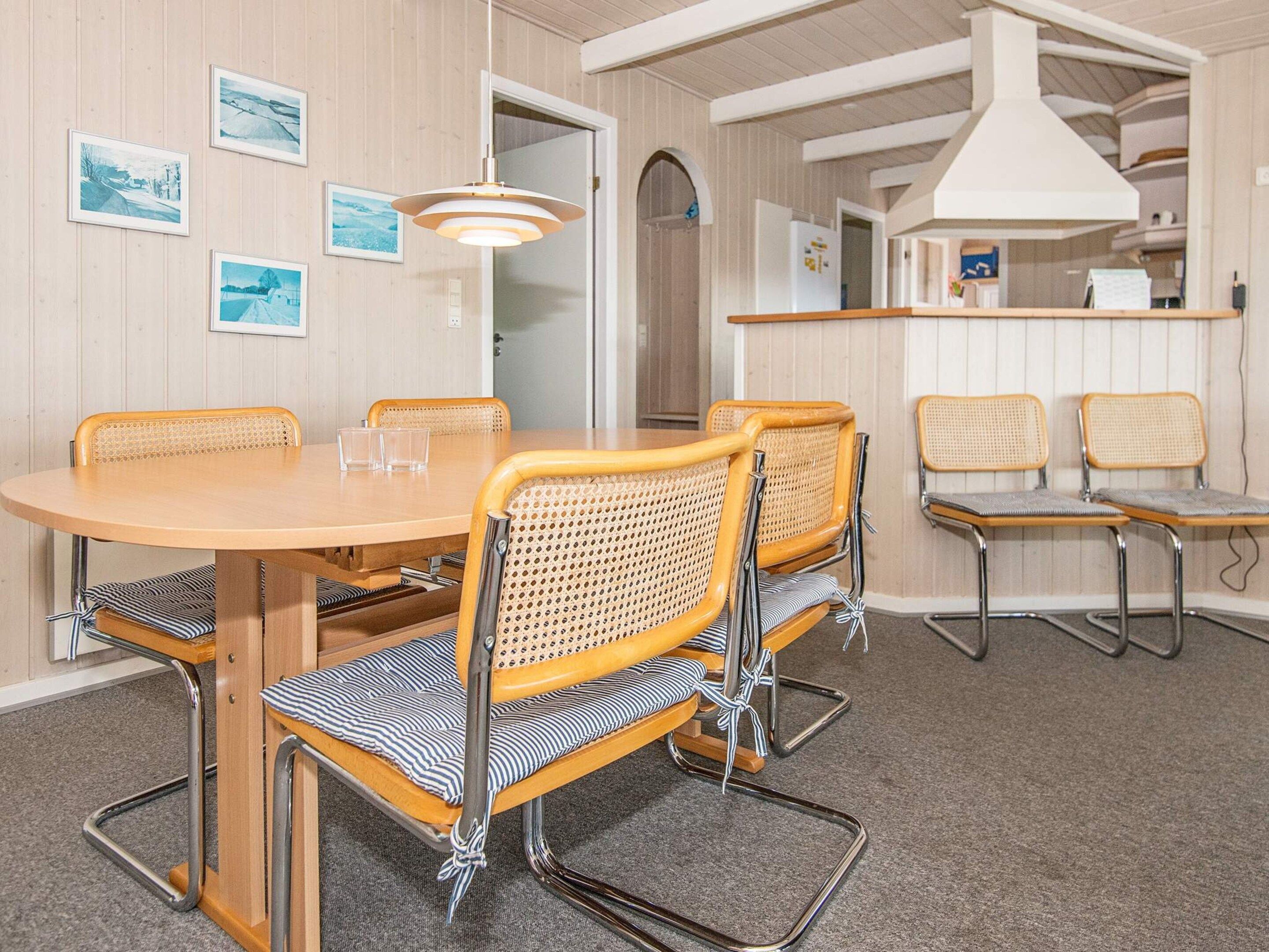 Un comedor con una mesa redonda y cuatro sillas, una cocina con estufa blanca, y un pasillo con una puerta.