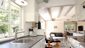 A modern kitchen with a large window, a coffee maker, a stove, and a dining area with a sofa and table. - 5 Person Holiday Home in Vejby (Vejby)