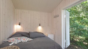 A bedroom with a bed, two wall-mounted lights, a bedside table, and a view of greenery outside. - 5 Person Holiday Home in Vejby (Vejby)