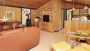 Een knus houten interieur met een leren bank, een eethoek en een keuken met houten kastjes.