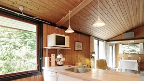 Een kleine keuken met houten wanden, een ingebouwde magnetron, een spoelbak en een eethoek met een tafel en stoelen.