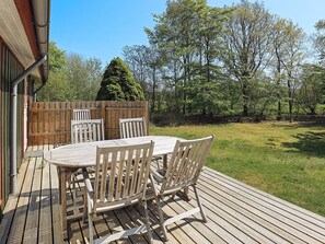 An outdoor deck with a wooden table and chairs, surrounded by a wooden fence and trees.