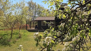Een klein huis met pannendak, omringd door weelderige begroeiing en bloeiende bomen.