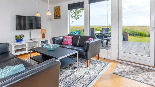 Un salon moderne comprenant un canapé, une table basse et un téléviseur, ainsi que de grandes portes-fenêtres coulissantes donnant sur un espace extérieur avec vue sur la mer.