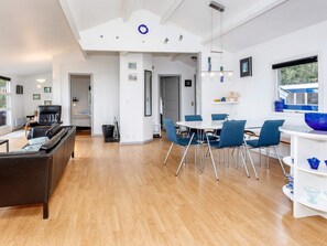 A modern living space with a sofa, dining table, and chairs, a kitchen area, and a large window. - 4 Star Holiday Home in Hadsund (Hadsund)