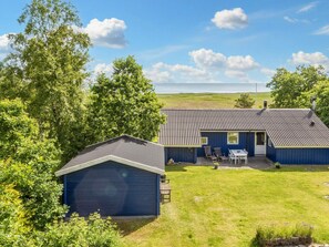 A blue house with a garage, a patio with chairs and a table, and a view of the sea. - 4 Star Holiday Home in Hadsund (Hadsund)