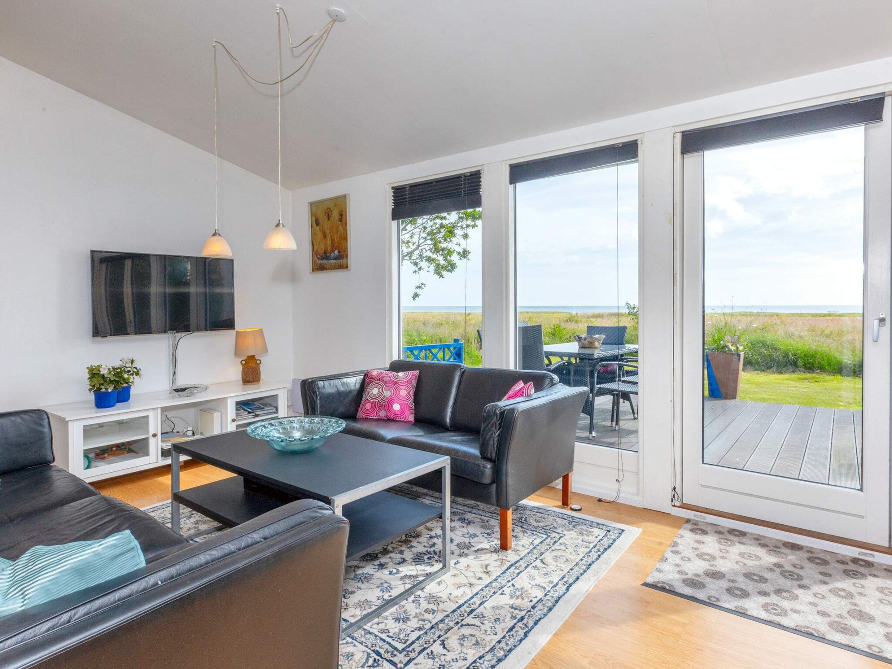 A modern living room with a sofa, coffee table, and a television. There is a large window offering a view of the outdoors.