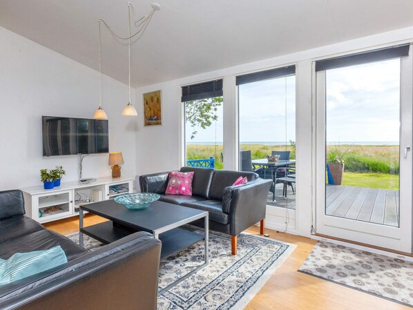 A modern living room with a sofa, coffee table, and a television. There is a large window offering a view of the outdoors. - 4 Star Holiday Home in Hadsund (Hadsund)