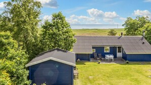 Une maison bleue avec un toit en métal, un garage et une terrasse aménagée avec du mobilier d’extérieur.