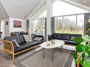 A modern living room with two black leather sofas, a round coffee table, and a large window offering a view of the outdoors.
