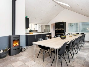A modern kitchen with a central island, a dining area with a long table and chairs, and a wood-burning stove.